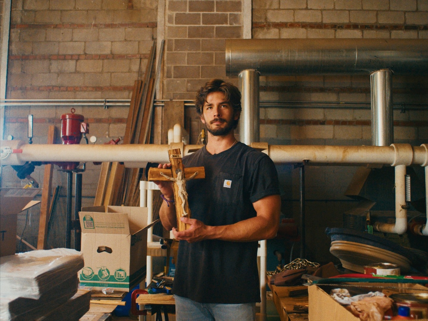 Danny Fisher standing in the workshop holding a handmade branch crucifix
